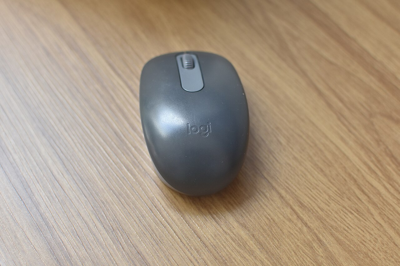 Foto real de um mouse Logitech M196 grafite sobre uma mesa de madeira