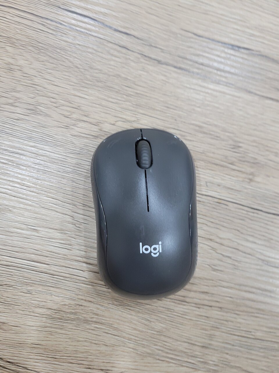 Foto real de um mouse Logitech M220 preto sobre uma mesa de madeira