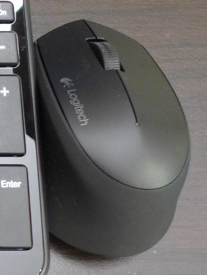 Foto real de um mouse Logitech M280 preto ao lado de um teclado